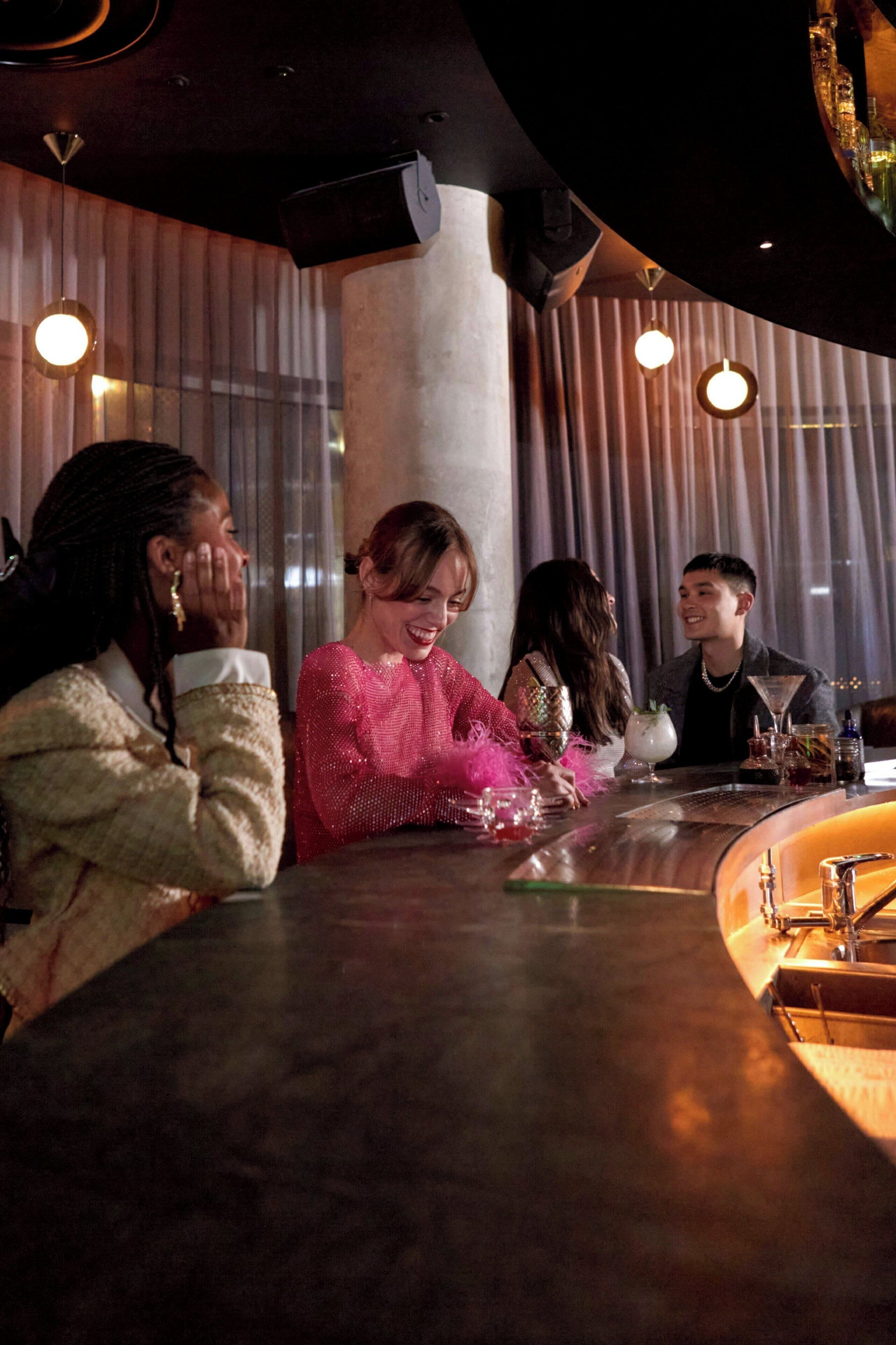 A group of people seated at a bar with a modern design, featuring a curved counter and pendant lighting.
