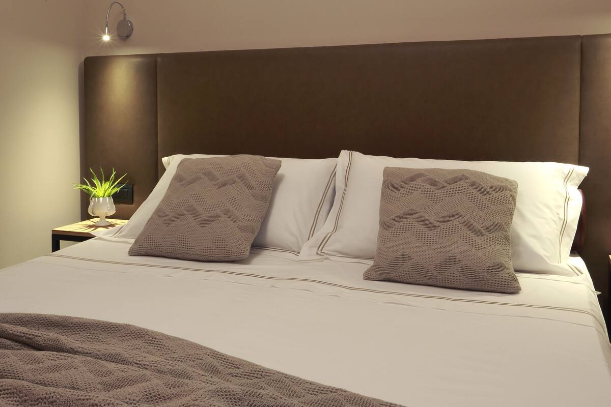 A neatly made bed with a brown headboard, white pillows, and a brown blanket.