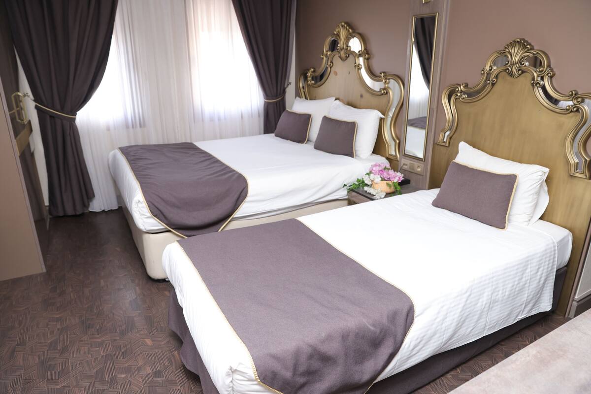 Une chambre d’hôtel avec deux lits, un grand miroir et une petite table sur laquelle est posé un vase de fleurs.
