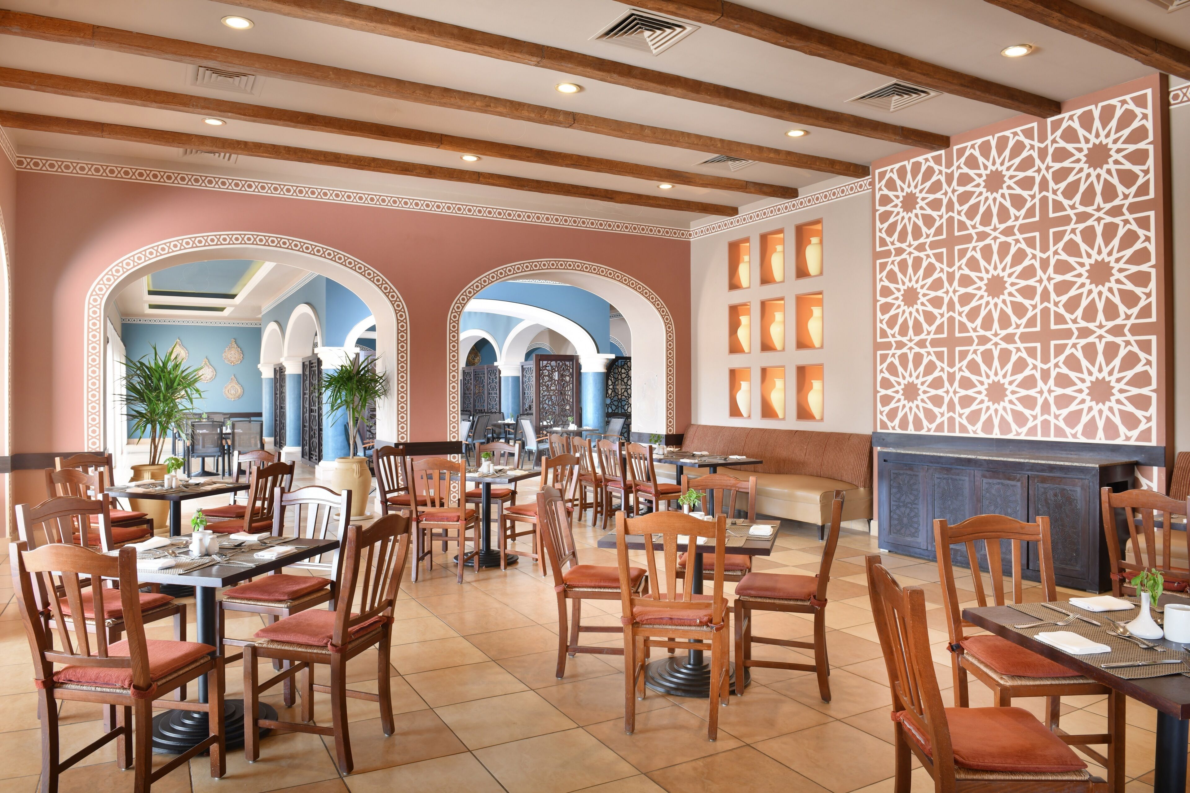 A spacious dining area with multiple tables and chairs, featuring a modern design with wooden furniture and decorative arches.