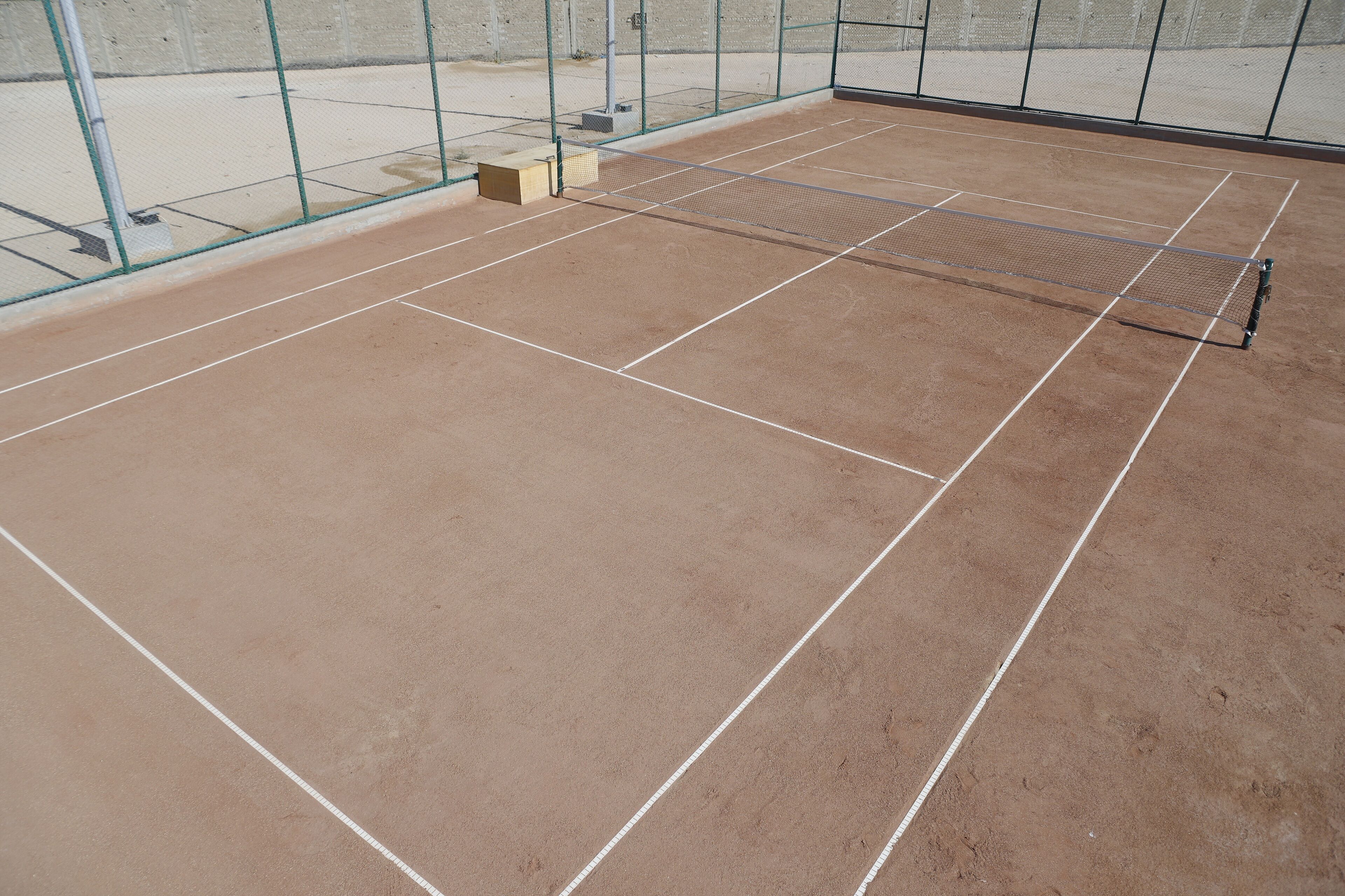 An indoor tennis court with a net, court lines, and a fence.