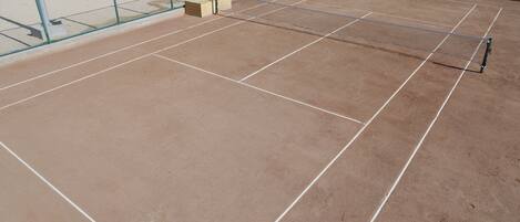 An indoor tennis court with a net, court lines, and a fence.