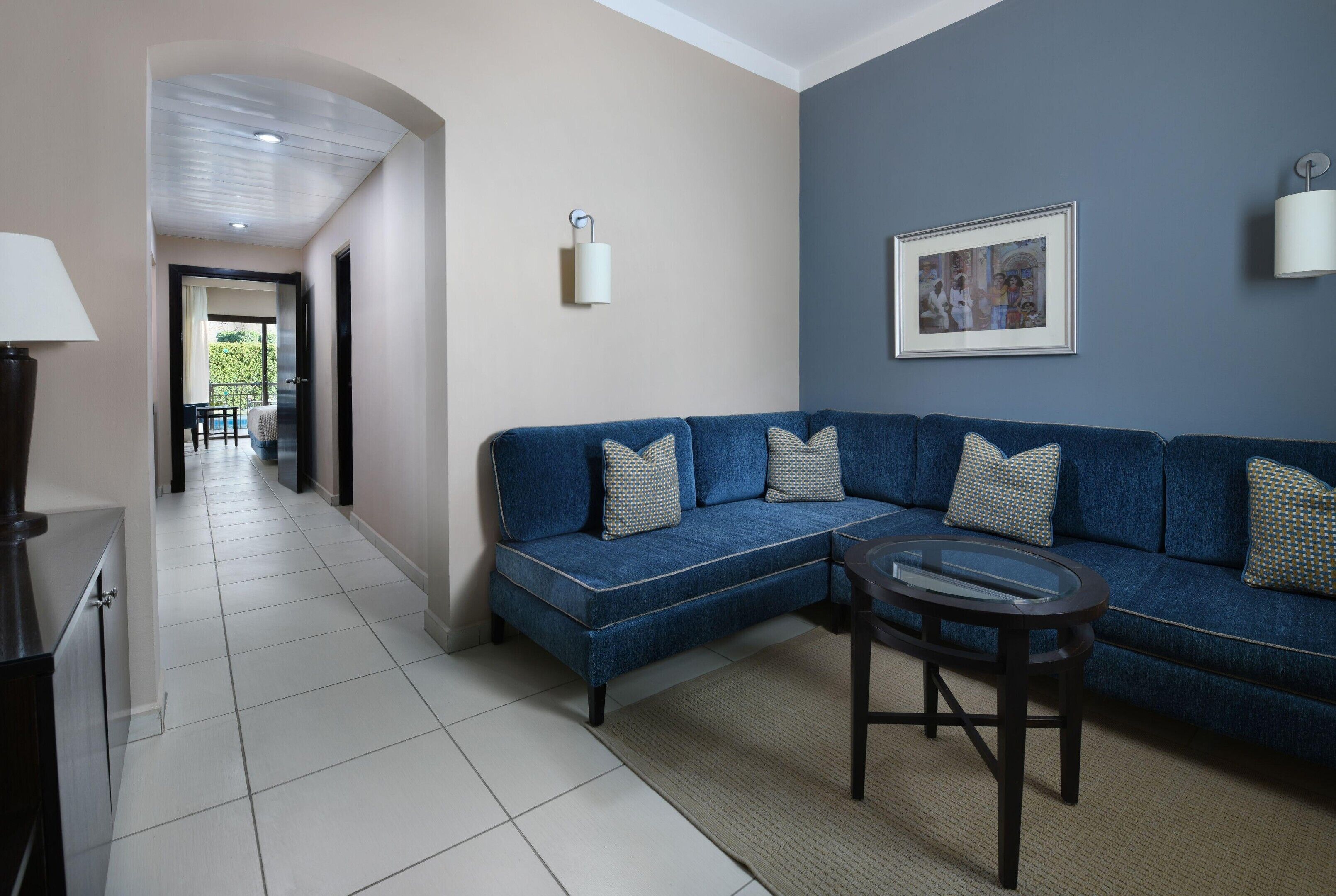 A modern living room with a blue sofa, a glass coffee table, and a framed picture on the wall.