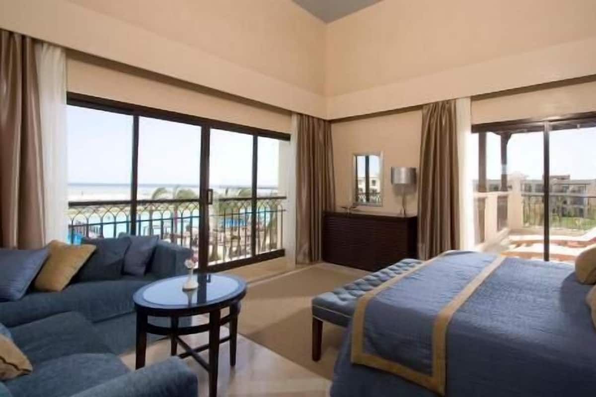 A hotel room with a balcony, a bed, a sofa, and a small table.