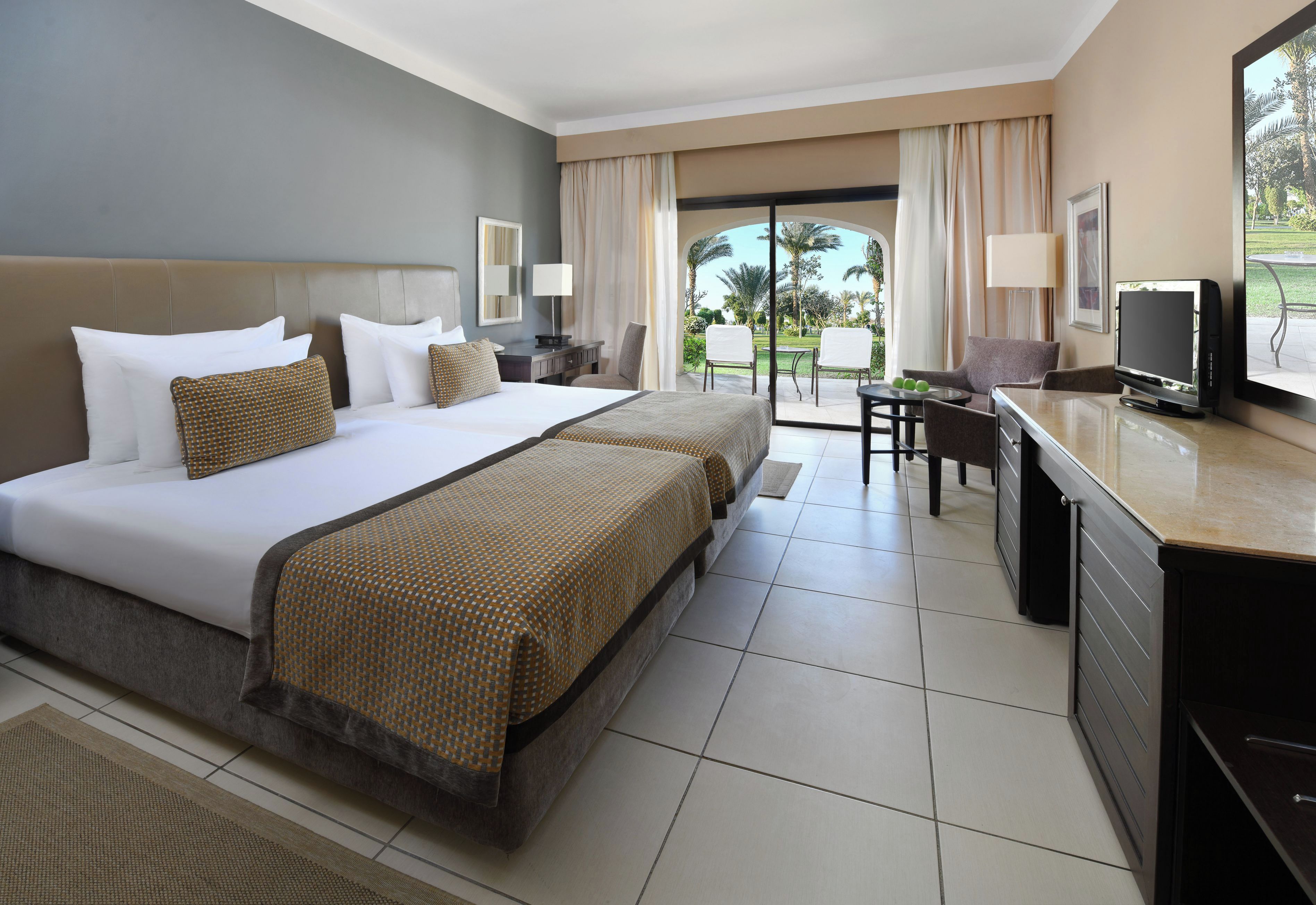 A hotel room with a large bed, a desk, a television, and a view of the outdoors.