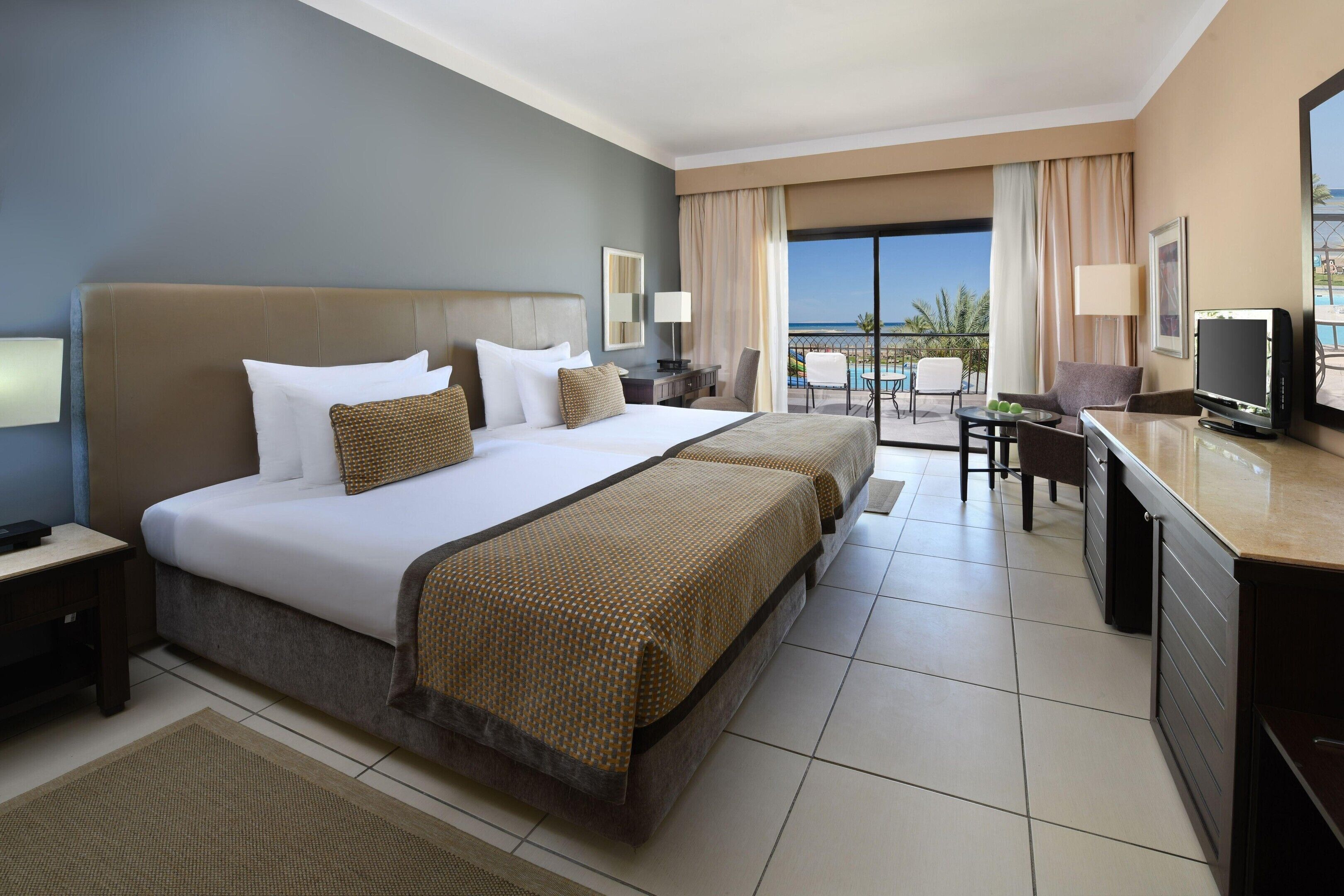 A hotel room with a large bed, a desk with a TV, and a balcony with a view.