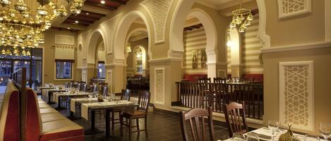 A restaurant with multiple dining areas, including a long communal table and individual tables, all set with tableware and chairs.