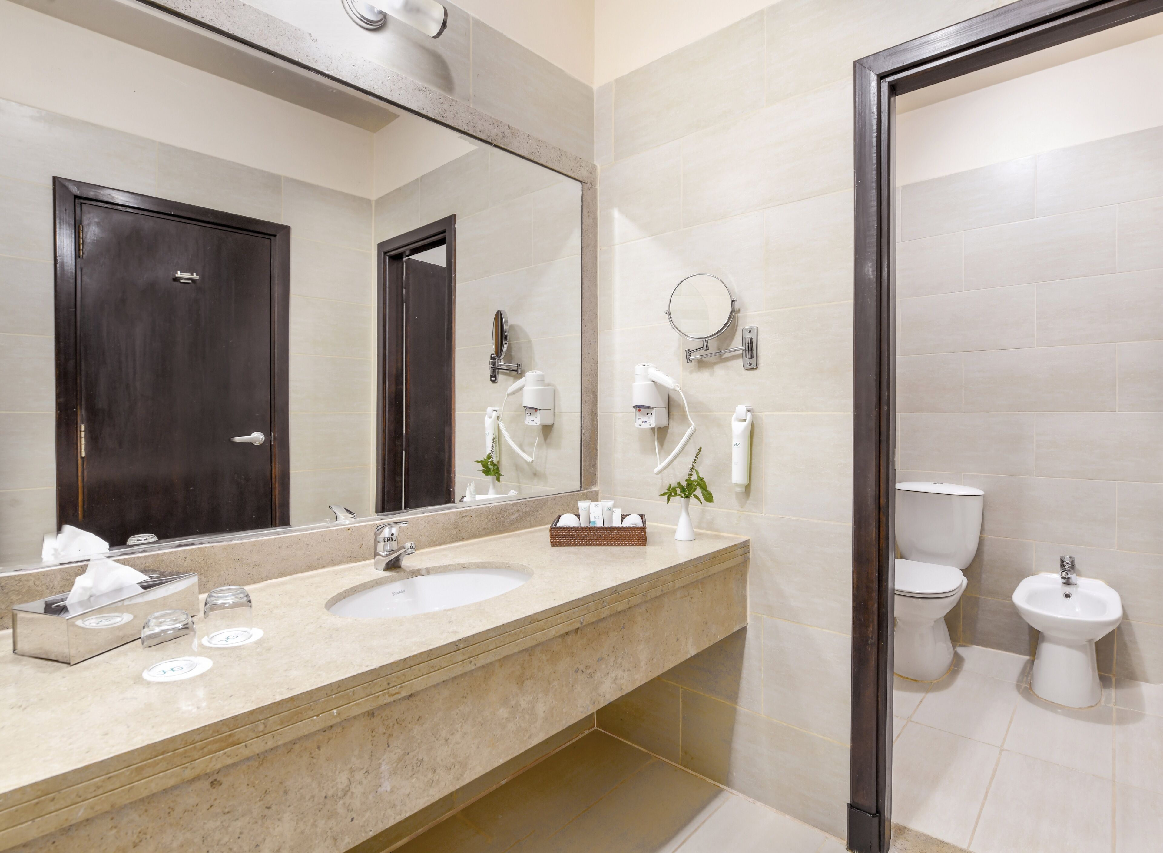 A modern bathroom with a large mirror, a sink, a toilet, and a bidet.