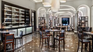 Un hall d’hôtel spacieux comprenant un bar, plusieurs espaces aménagés pour s’asseoir et une grande bibliothèque.