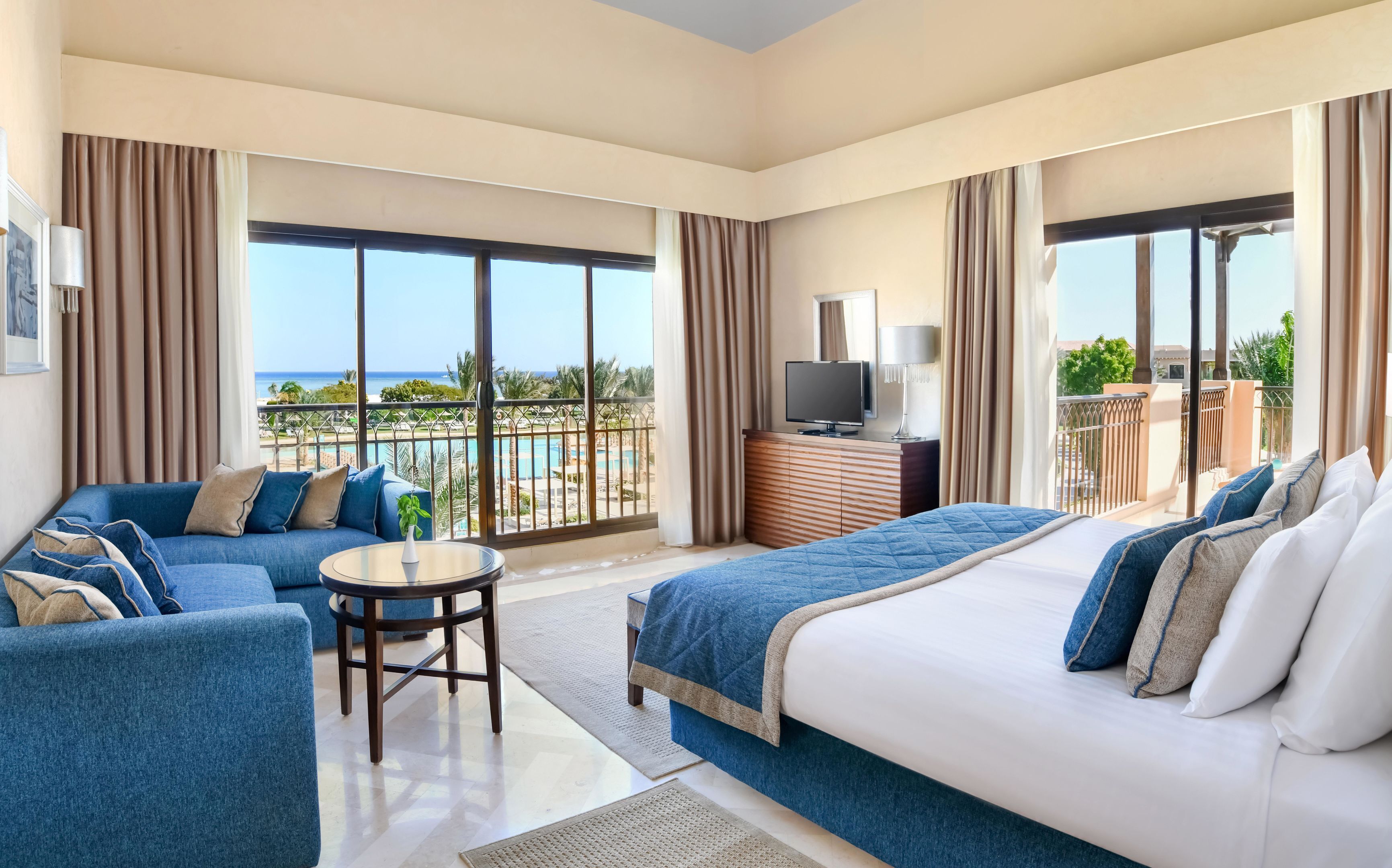 A hotel room with a balcony, a bed, a sofa, a TV, and a small table.