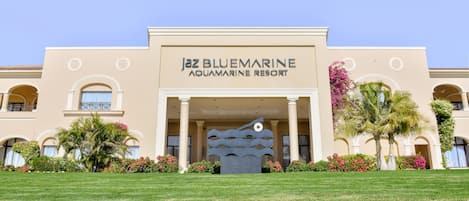 The exterior of the BlueMarine Aquamarine Resort with a clear entrance, palm trees, and a decorative wave sculpture.