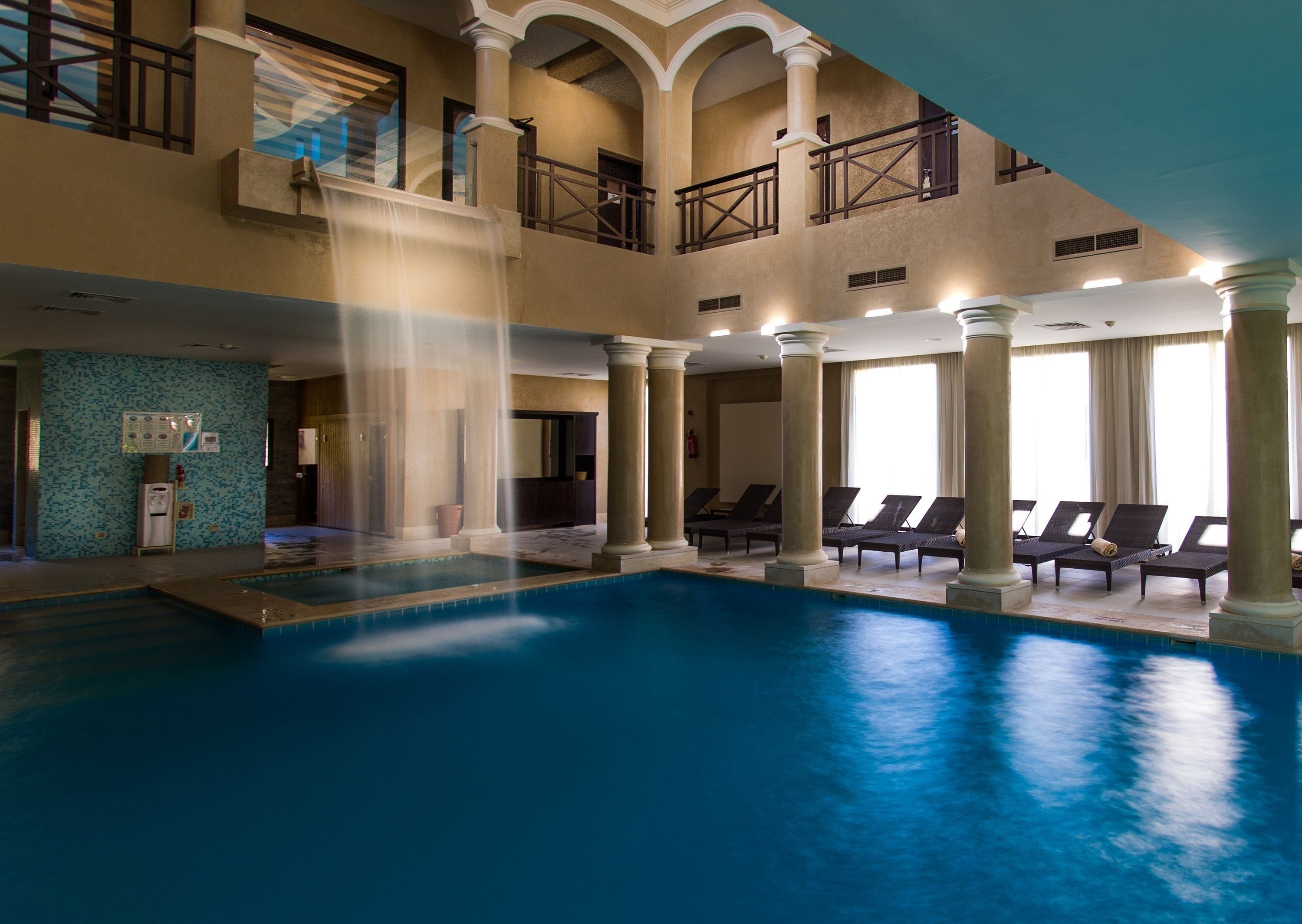 A large indoor swimming pool with multiple lounge areas and a water fountain feature.
