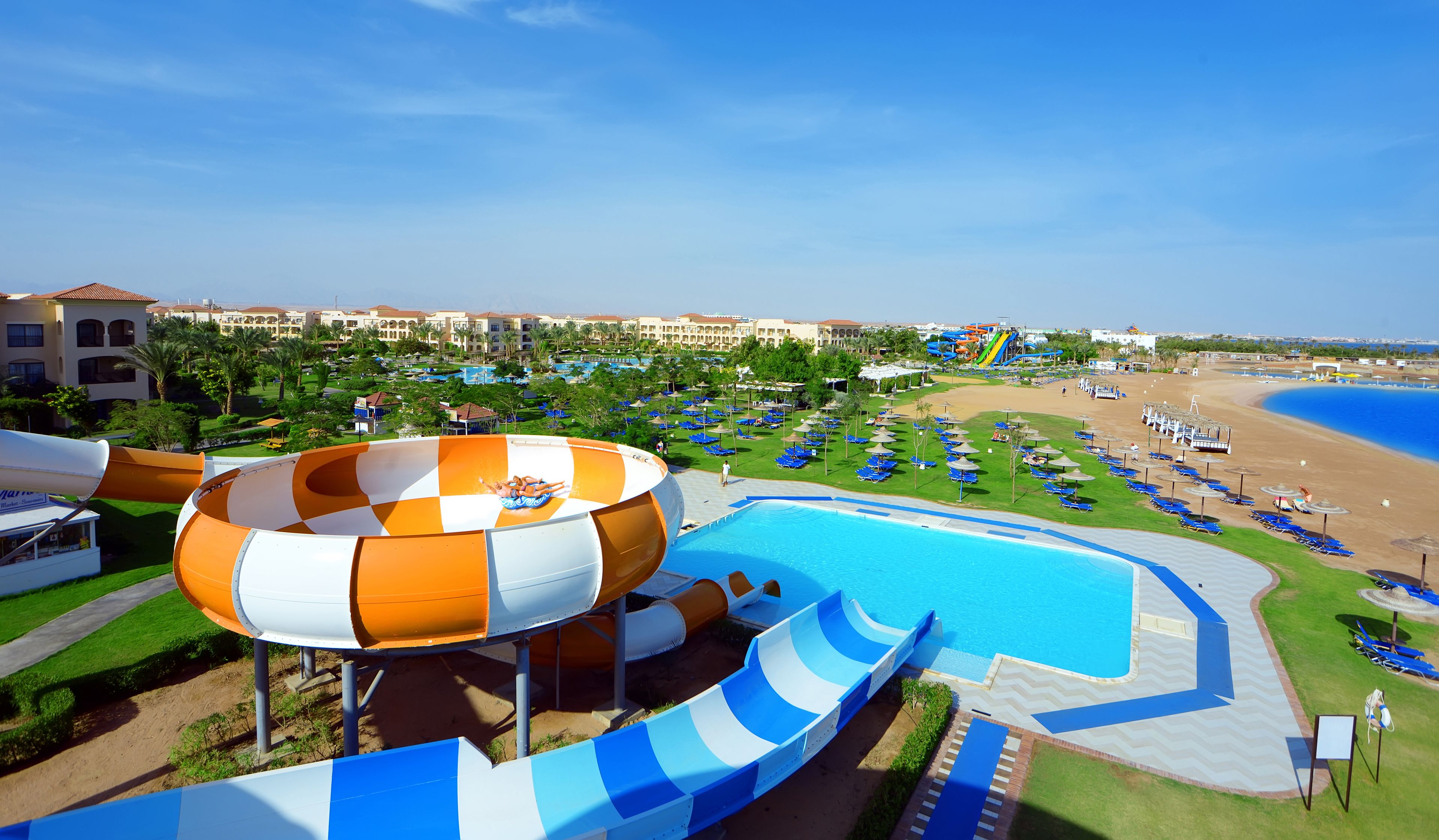 A water park with a large water slide, a pool, and a beach area with lounge chairs.