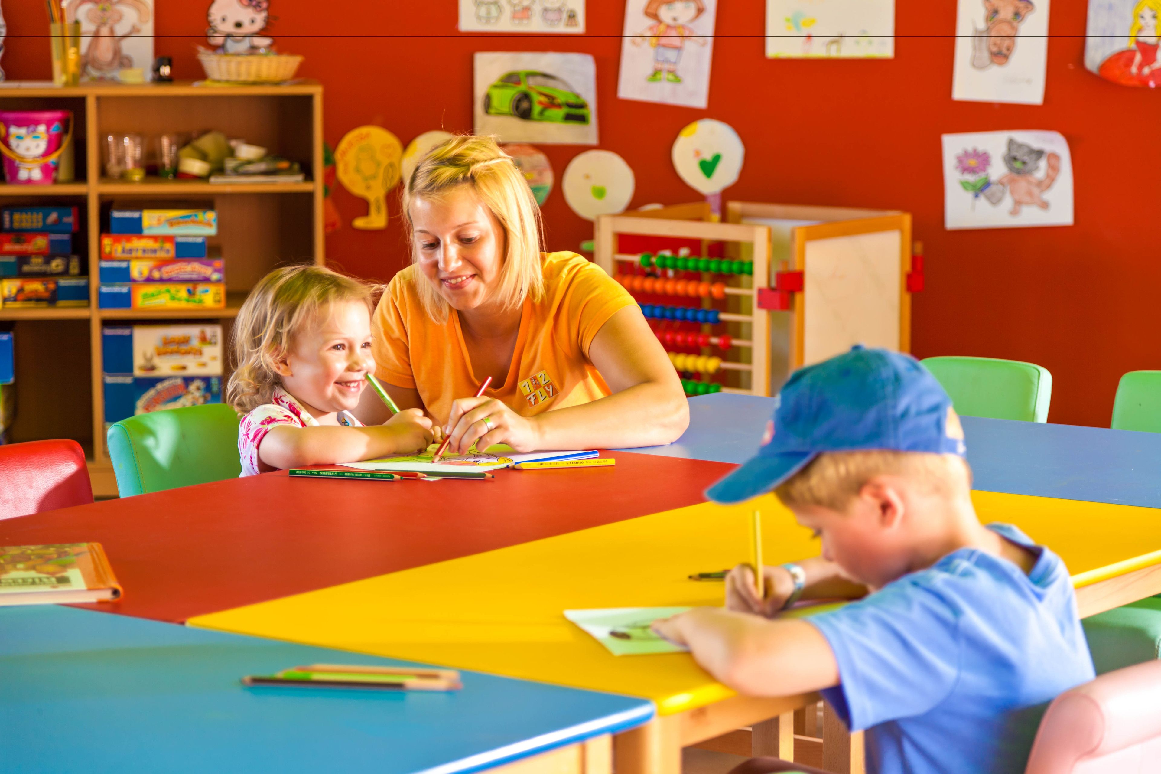 A classroom with children and an adult at a table, surrounded by educational materials and colorful decorations.