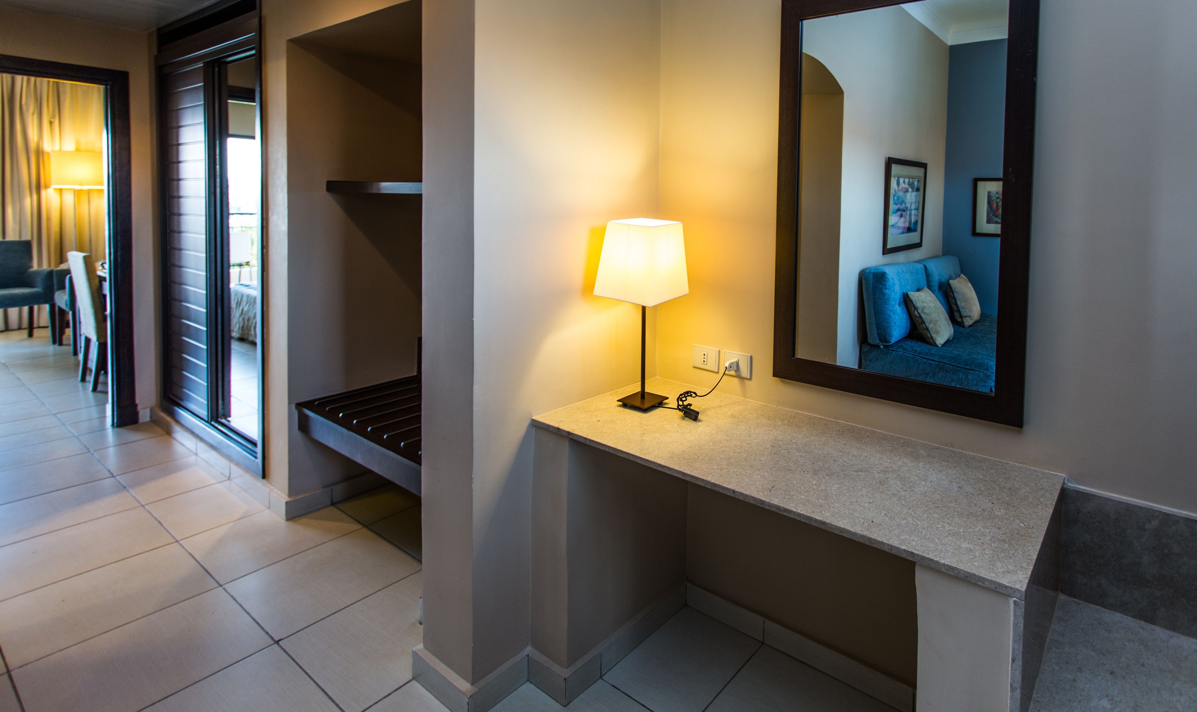 A hotel hallway with a lamp, a mirror, and a seating area in the background.