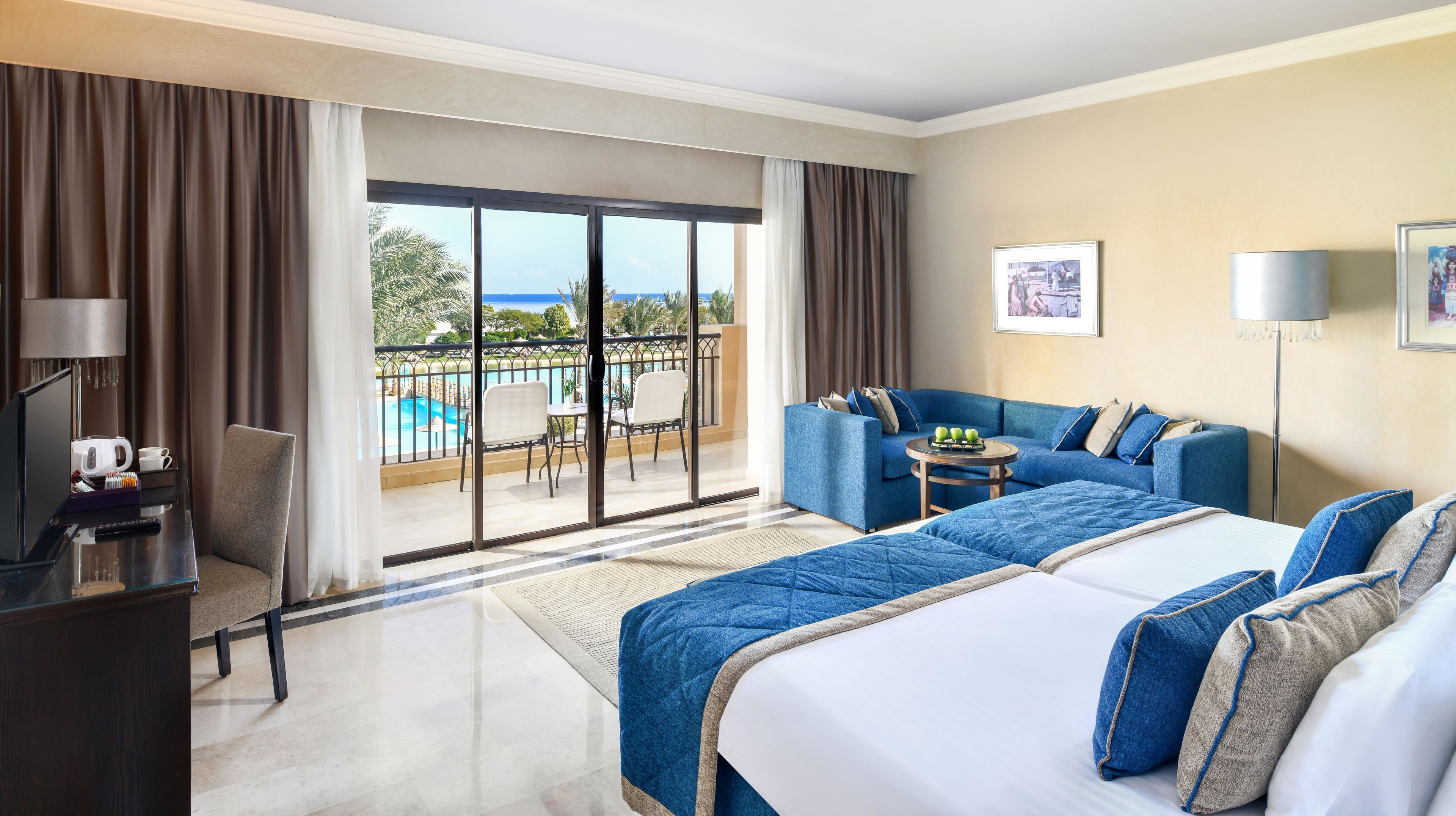 A hotel room with a bed, a sofa, a desk, a chair, a small table, and a balcony with a pool view.