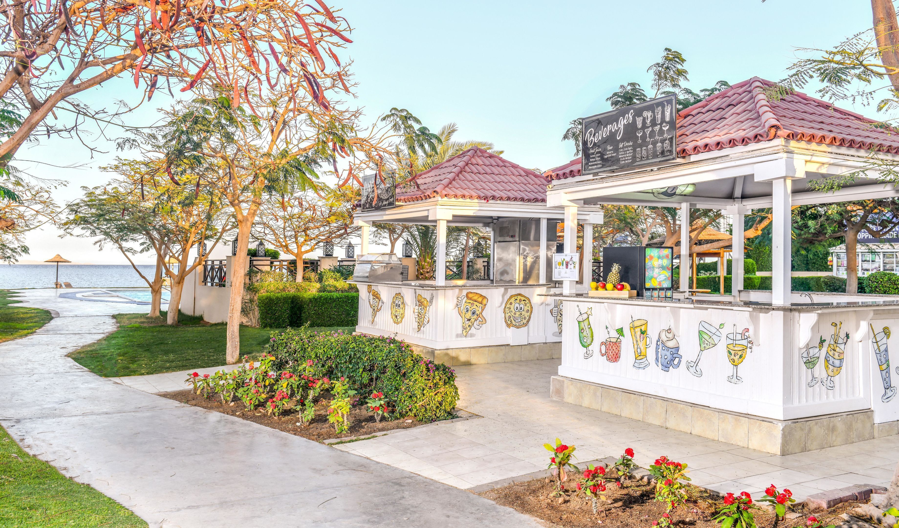 A seaside restaurant with outdoor seating, a signboard listing beverages, and a view of the ocean.