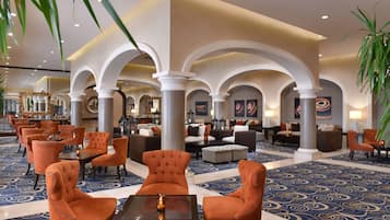 A spacious lobby with a blue patterned carpet, orange upholstered chairs, and a central seating area with sofas and tables.