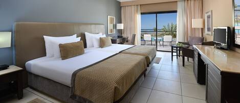 A hotel room with a large bed, a desk, a TV, and a balcony with a view of the ocean.