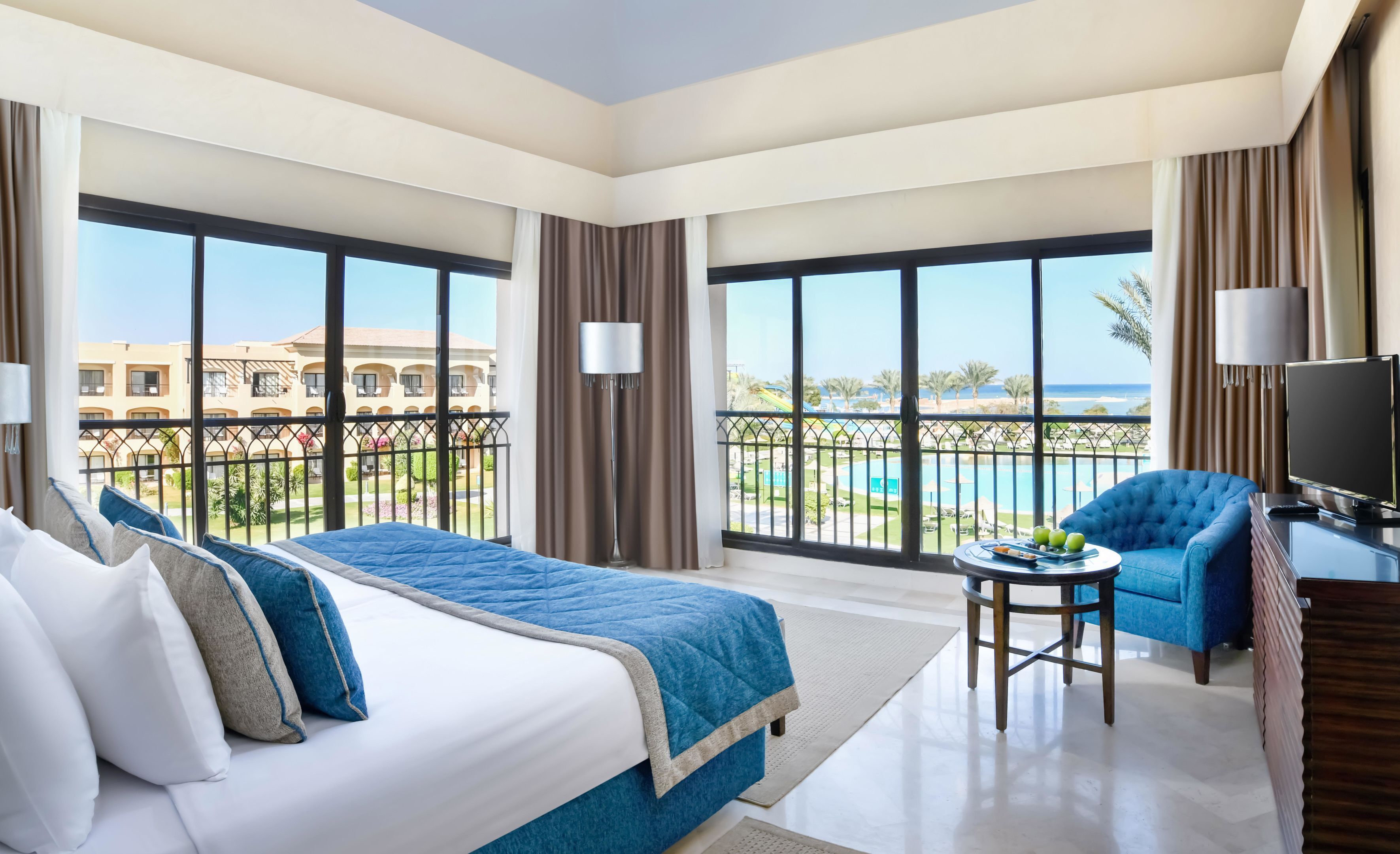 A hotel room with two beds, a TV, a small table with fruit, and a balcony with a pool view.