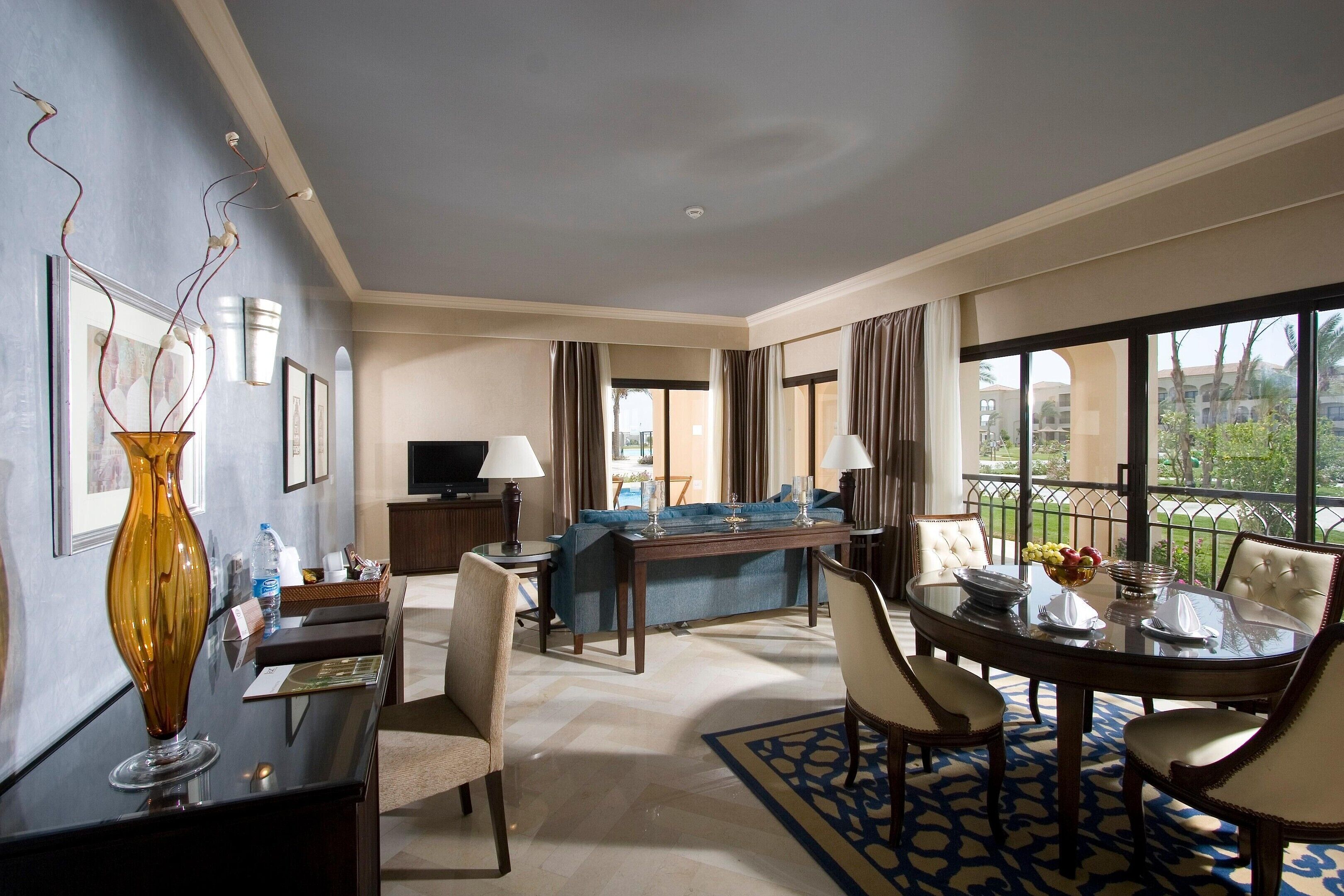 A hotel room with a dining area, a sofa, a TV, and a view of the outdoors.