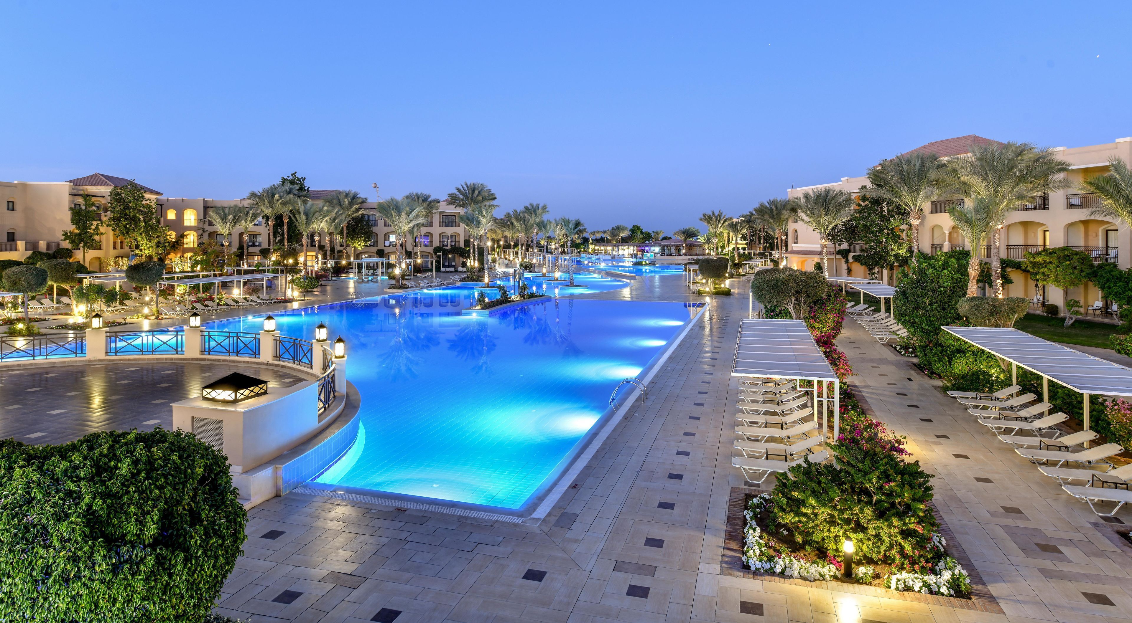 A large swimming pool with a surrounding walkway, palm trees, and lounge chairs.