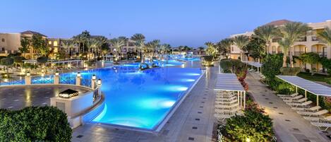A large swimming pool with a surrounding walkway, palm trees, and lounge chairs.