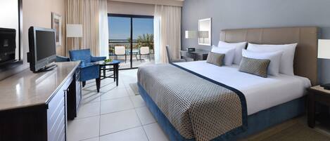 A hotel room with a bed, a desk, a chair, a TV, and a balcony with a view.