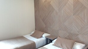 Ein Hotelzimmer mit zwei Einzelbetten, einem kleinen Tisch und einer Wand mit geometrischem Muster.