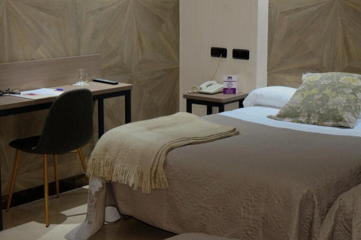 A hotel room with a bed, a desk, a chair, a phone, and a wall with a geometric pattern.