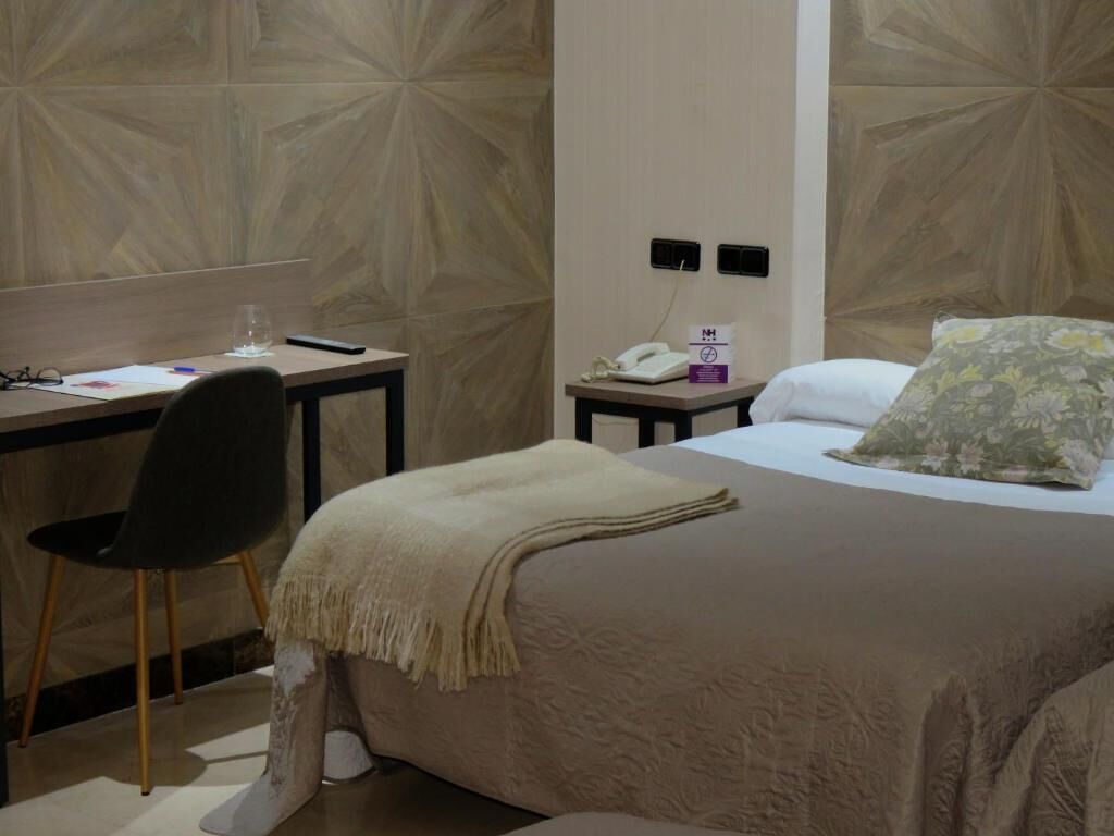 Una habitació d'hotel amb un llit, una taula de treball, una cadira, un telèfon i una paret amb un disseny geomètric.