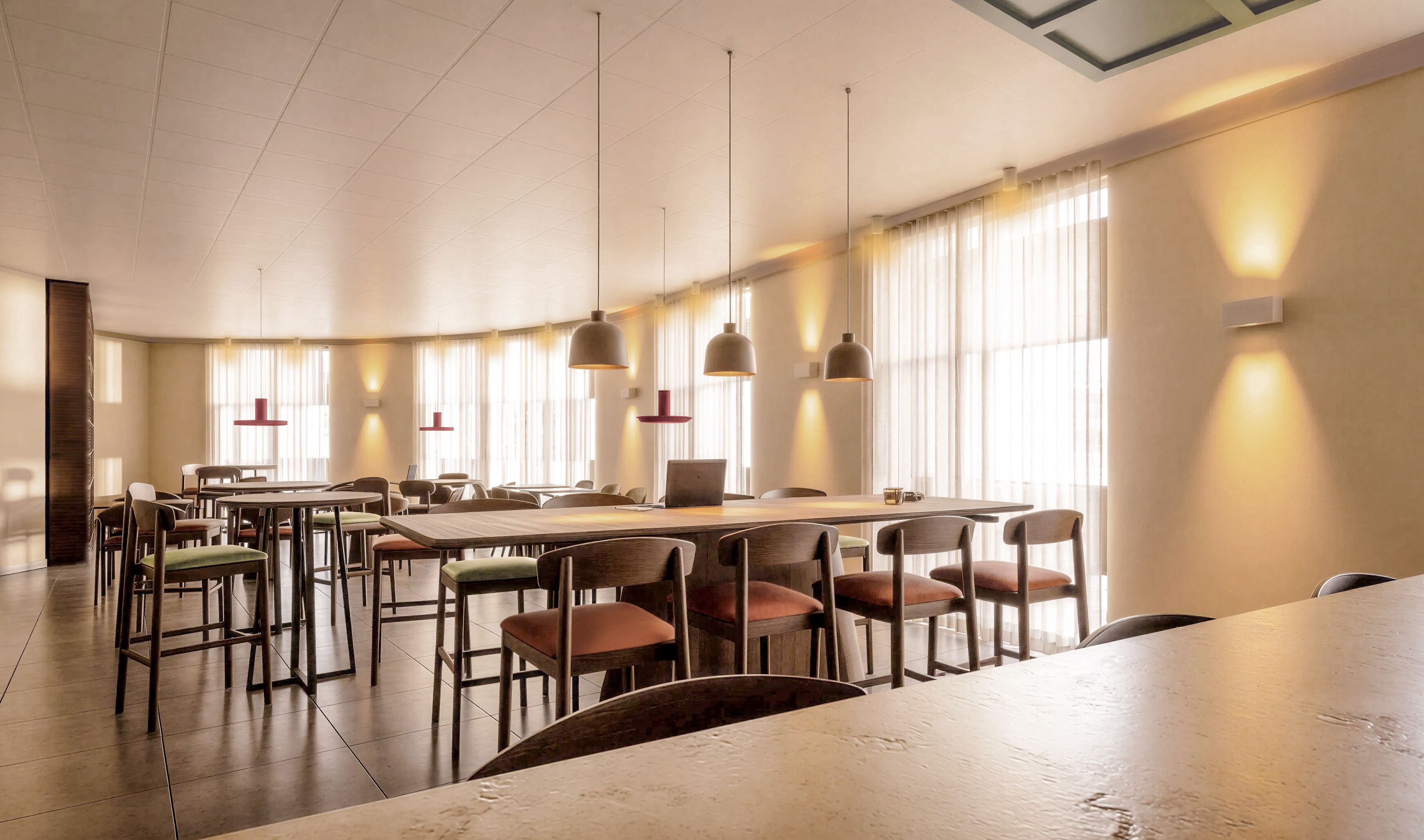 A spacious conference room with a long table, multiple chairs, pendant lights, and large windows with sheer curtains.