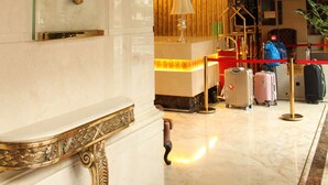 Un vestíbulo de hotel con suelo de mármol, un mostrador de recepción, un perchero y un elemento decorativo en la pared.