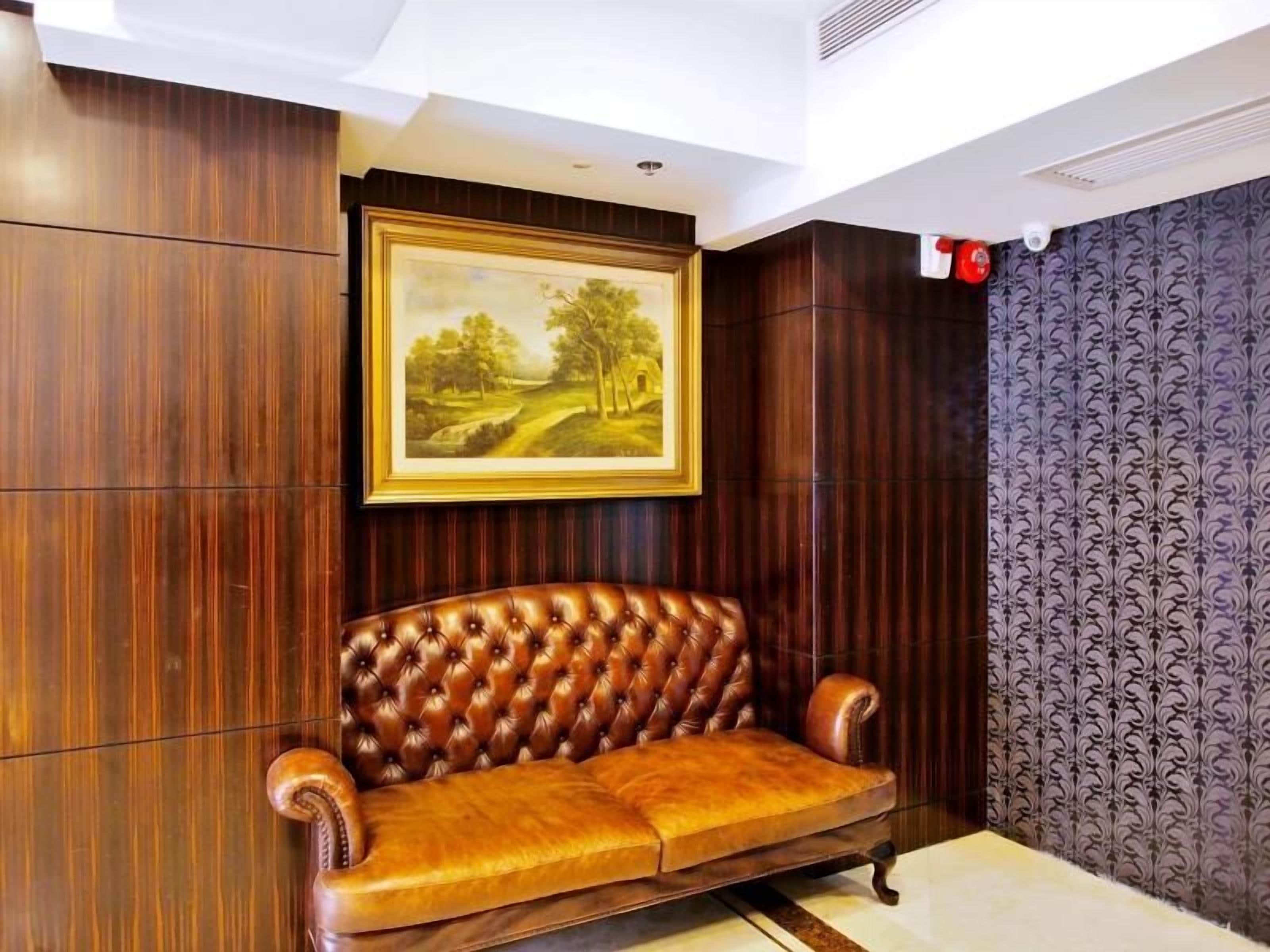 A room with a brown leather sofa, a framed landscape painting, wooden paneling, and patterned wallpaper.
