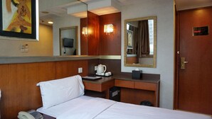 Habitación de hotel con una cama, un escritorio con teléfono, cafetera y espejo.