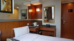Habitación de hotel con una cama, un escritorio con teléfono, cafetera y espejo.