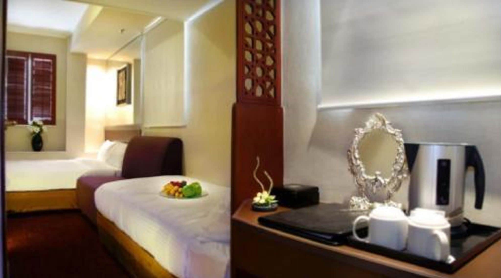 A hotel room with a bed, a bedside table with a coffee maker, and a decorative mirror.