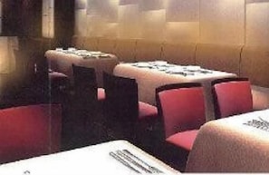 L'intérieur d'un restaurant, avec des banquettes et des tables, dont certaines sont dotées de coussins rouges.