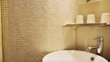 A bathroom with a tiled wall, a sink, and a shelf with stacked cups.