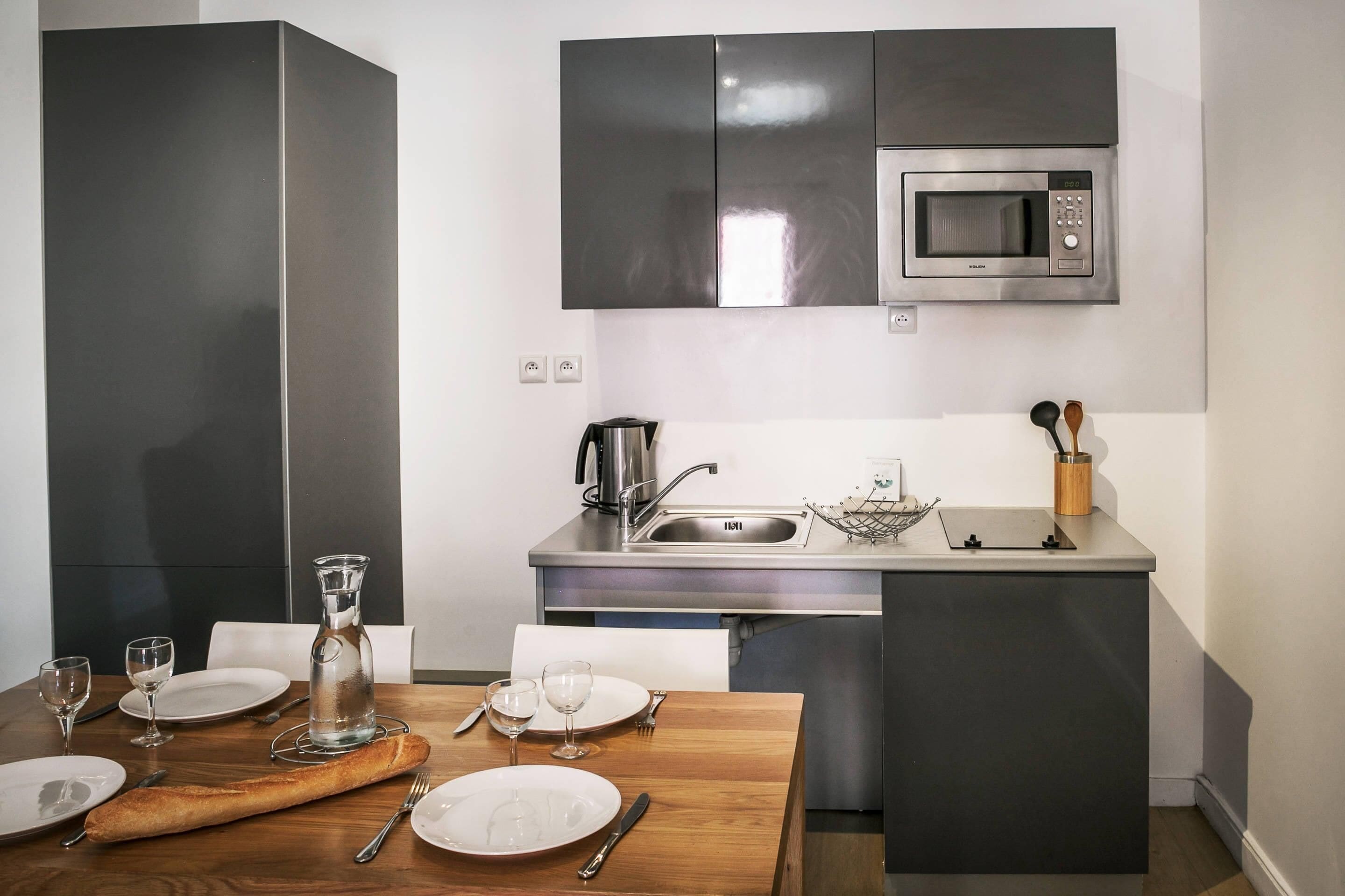 A compact kitchen with a microwave, sink, and a small dining area with a wooden table set for two.