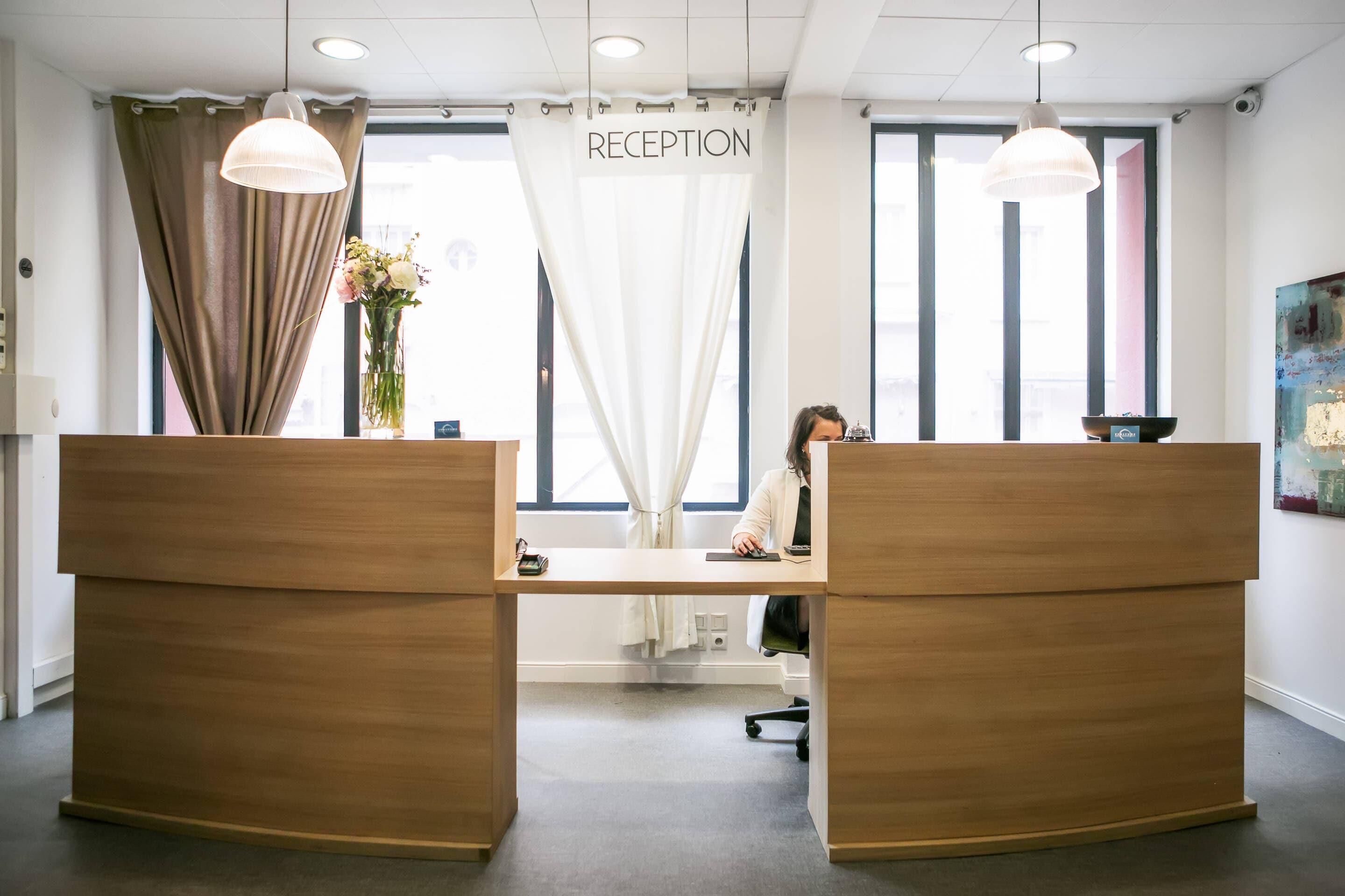 A reception desk with a sign, a vase with flowers, and a large window with curtains.