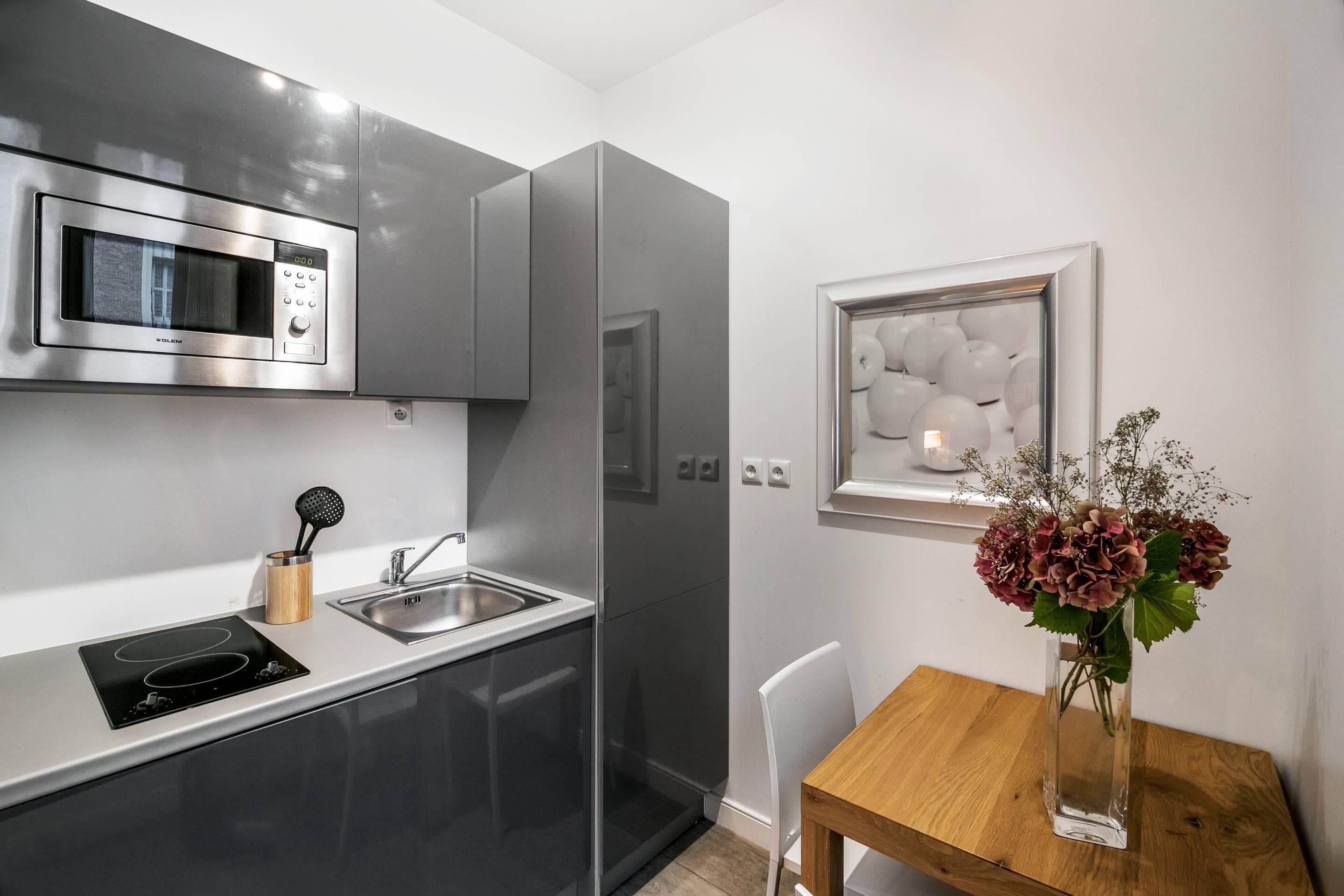 A modern kitchen with a built-in microwave, stainless steel appliances, a sink, and a wooden table with a vase of flowers.