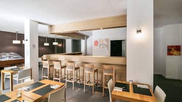 Interior modern d'un restaurant amb taules i cadires de fusta, una barra central i il·luminació penjant.