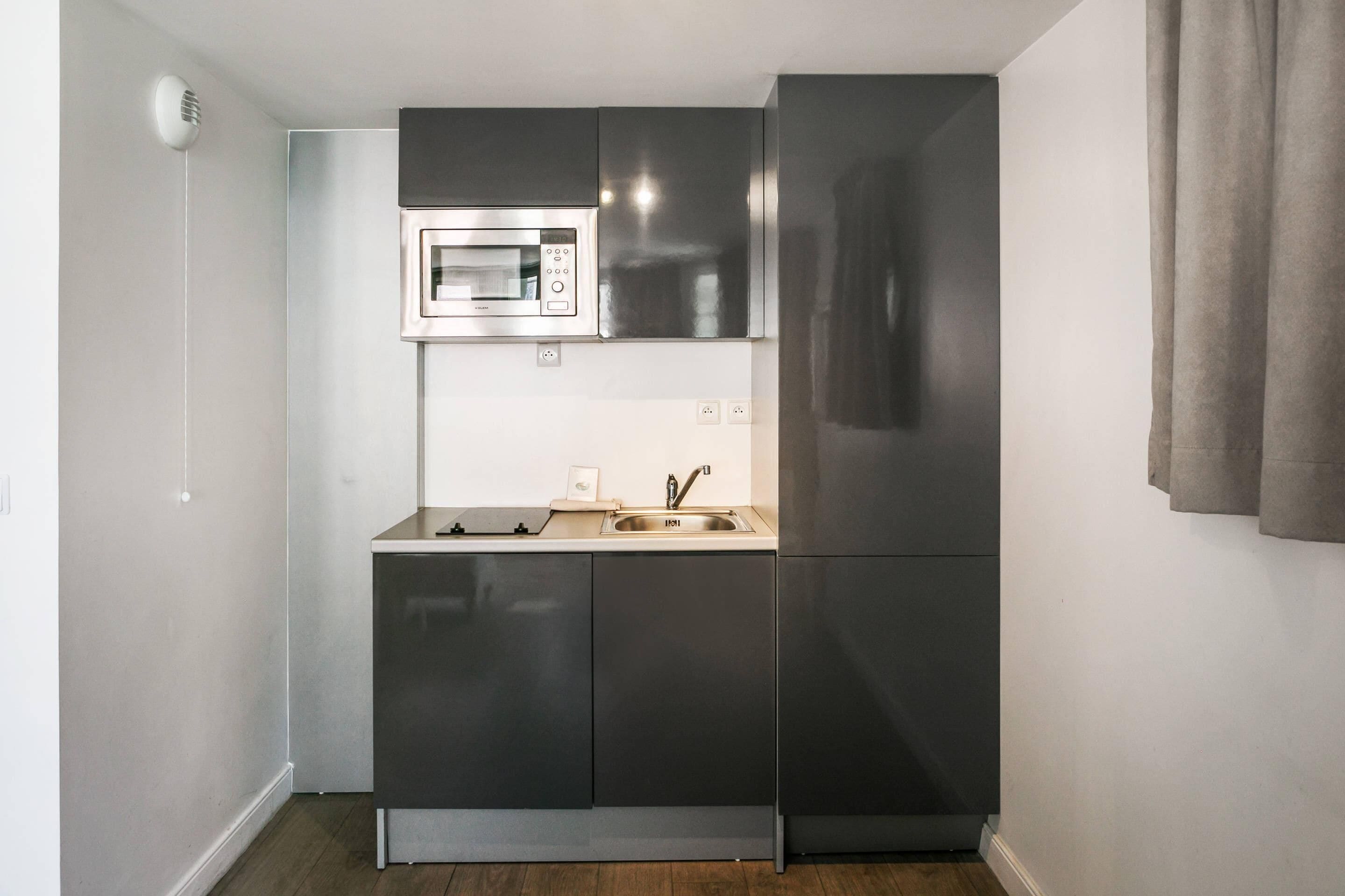A compact kitchen with a built-in microwave, stainless steel cabinets, and a sink.