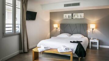 Habitación de hotel con cama, lámparas de noche, televisor montado en la pared y ventana con cortinas.