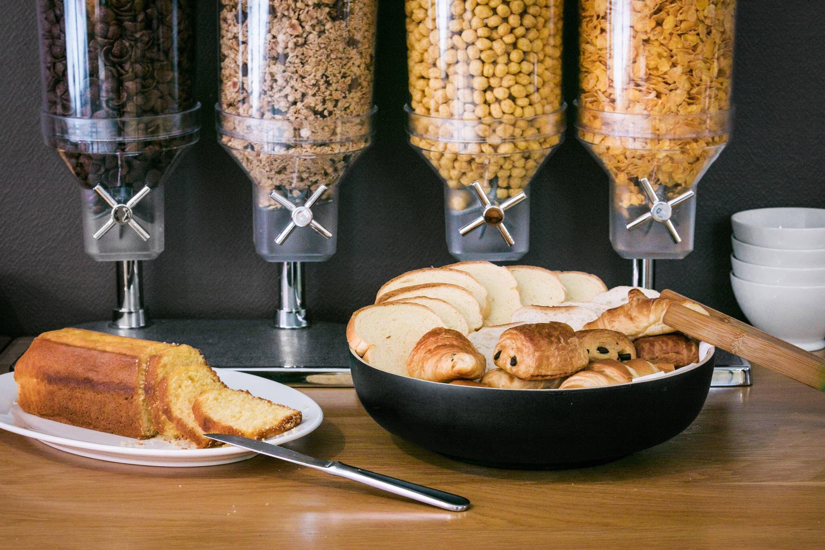 A breakfast setting with a loaf of bread, croissants, and a bowl of pastries on a table.