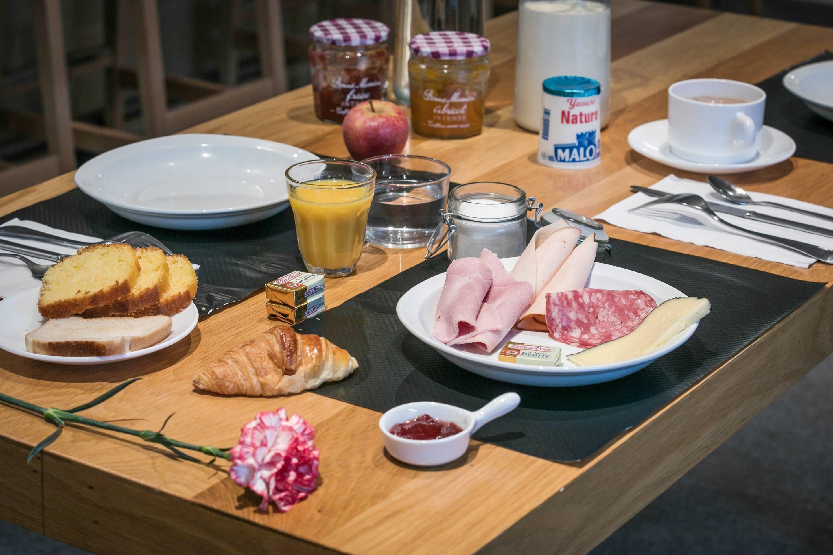 A breakfast table with plates of food, including croissants, ham, and cheese, along with condiments, a glass of orange juice, and a cup of coffee.