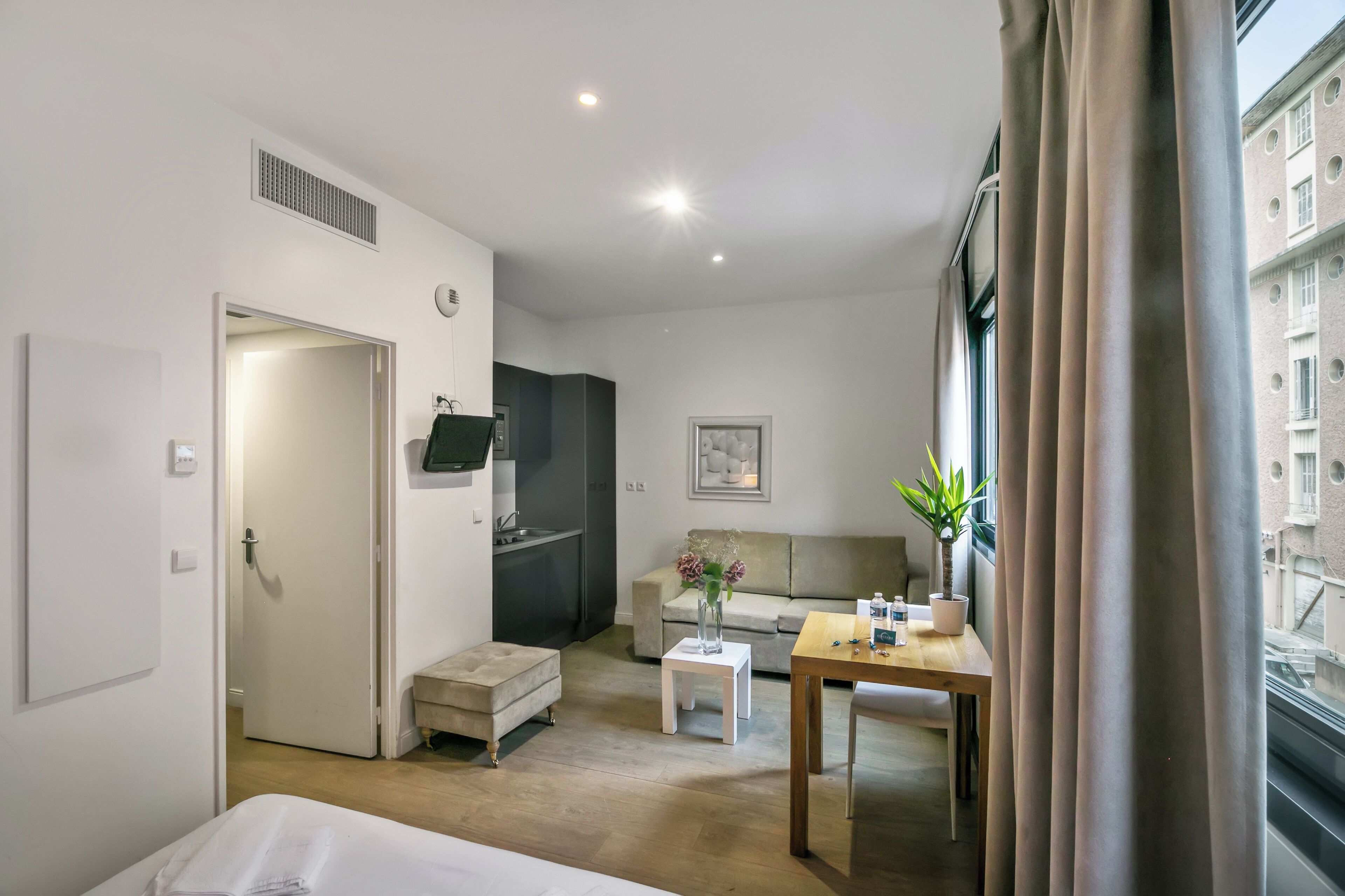 Ein Hotelzimmer mit Bett, einem kleinen Tisch, einer Couch, einer Küchenzeile und einem Fenster mit Vorhängen.