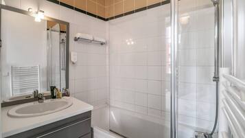 A modern bathroom with a large mirror, two sinks, a shower, and a bathtub.
