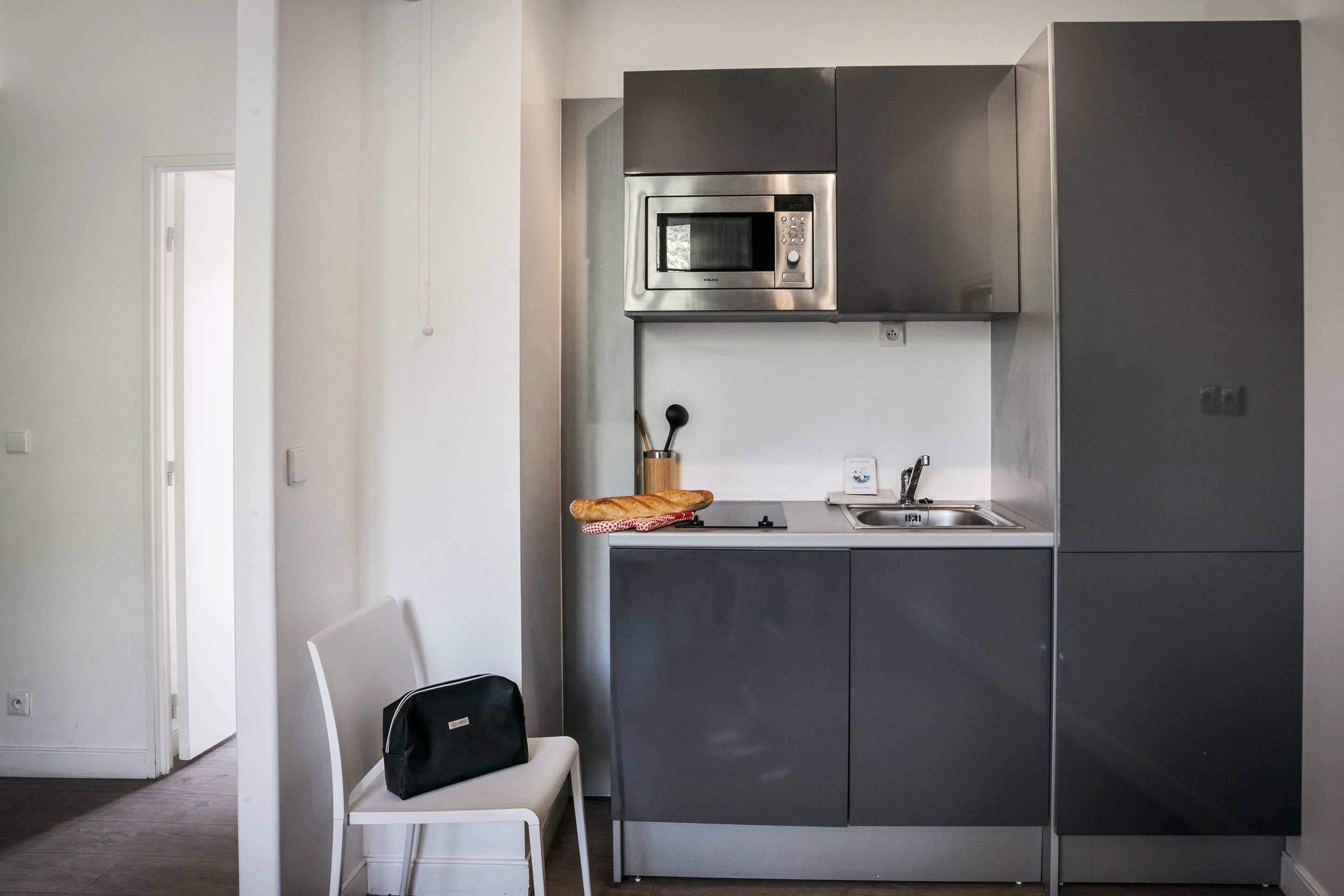 Una cocina compacta con microondas integrado, un lavabo y una pequeña encimera.